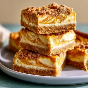 Creamy pumpkin cheesecake bars topped with whipped cream and a sprinkle of cinnamon.